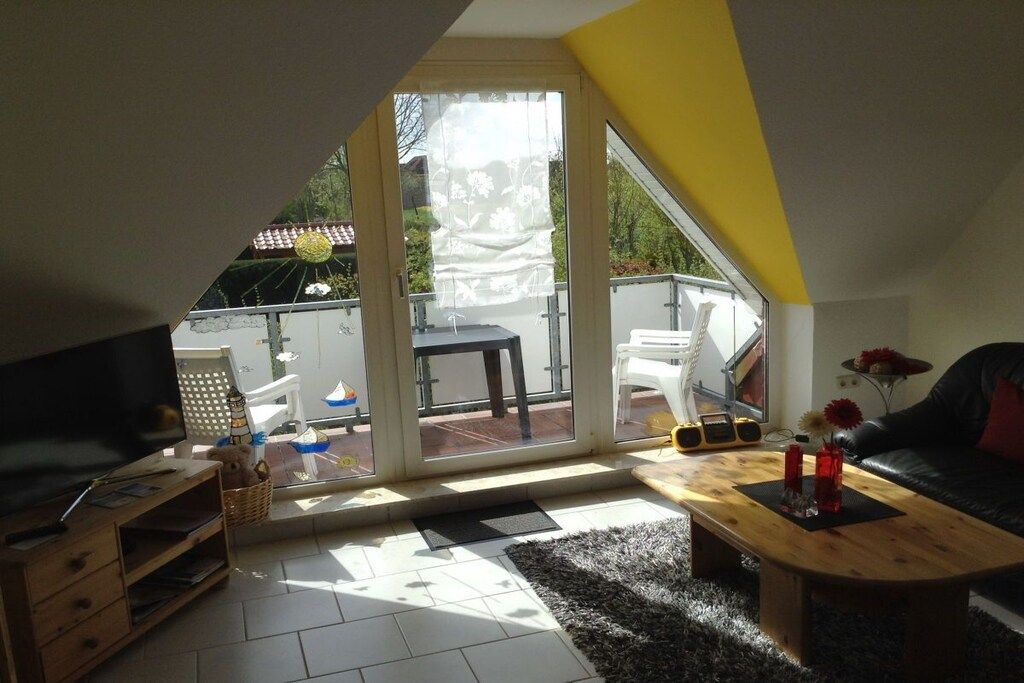 A living room with a TV, sofa, coffee table, and a view through a glass door to an outdoor area with a table and chairs.