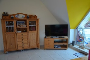 Ein Zimmer mit einem Holzkasten mit Schubladen und Regalen, einem Fernseher auf einem Schrank und einem Fenster mit Blick nach draußen.