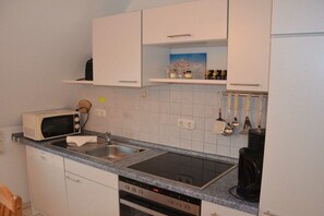 Una cocina compacta con gabinetes blancos, microondas, estufa y cafetera.