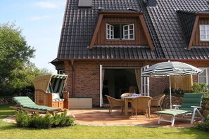 Una casa con techo inclinado, fachada de ladrillo y un patio con mobiliario exterior.
