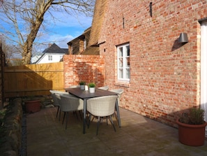A brick patio with a table and chairs, a wooden fence, and a potted plant. - 1 Aruba at Haus Boldix (Wyk auf Foehr)