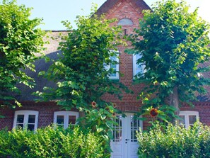 A brick house with a white door, surrounded by lush greenery and a clear sky. - 1 Aruba at Haus Boldix (Wyk auf Foehr)