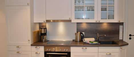 Cocina moderna con armarios blancos, horno empotrado, cafetera y vitrina con vajilla.