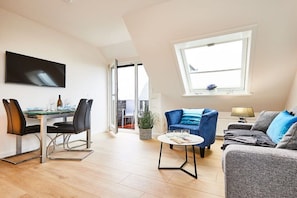 Ein modernes Wohnzimmer mit Essbereich, einer Couch, einem Fernseher und einem Fenster.
