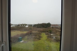 A view through a window of a grassy area with a path, a small structure, and buildings in the distance. - Holiday apartment with 2 bedrooms (Wenningstedt)