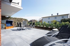An outdoor patio with a table and chairs, a blue sofa, and a large window overlooking a garden. - Holiday apartment in Sylt with 3 bedrooms (Westerland)