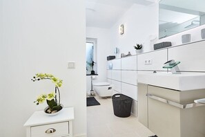 Une salle de bain moderne avec un lavabo blanc, un miroir et une petite plante orchidée.