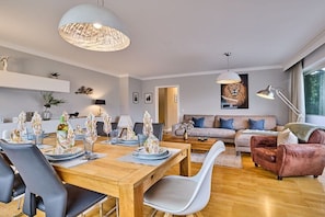 A modern living room with a dining area, featuring a wooden dining table, chairs, a sofa, and a coffee table. - Holiday apartment in Sylt with 3 bedrooms (Westerland)