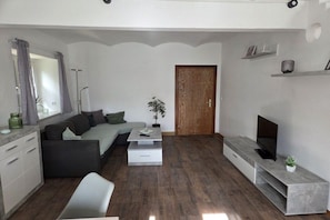 A modern living room with a sofa, coffee table, TV stand, and a door leading to another room. - Holiday apartment Hilmersdorf (Hilmersdorf)