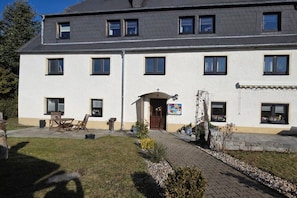 A two-story building with a paved entrance, outdoor seating, and a small garden area. - Holiday apartment Hilmersdorf (Hilmersdorf)
