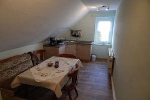 A compact kitchen with a dining table set for two, a window with a view, and a radiator. - Holiday apartment with 1 bedroom (Ebersbach-Neugersdorf)