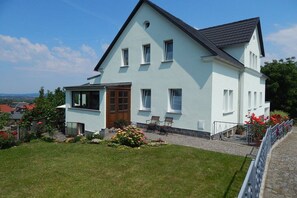 A two-story house with a balcony, a wooden door, and a garden with flowers. - Holiday apartment with 1 bedroom (Ebersbach-Neugersdorf)