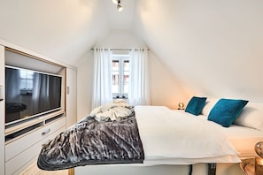 Ein Schlafzimmer mit einem Bett, einem Fernseher und einem Fenster mit Vorhängen.