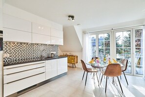 A modern kitchen with white cabinets, a tiled backsplash, and a dining area with a table and chairs. - Holiday apartment with 3 bedrooms (Westerland)