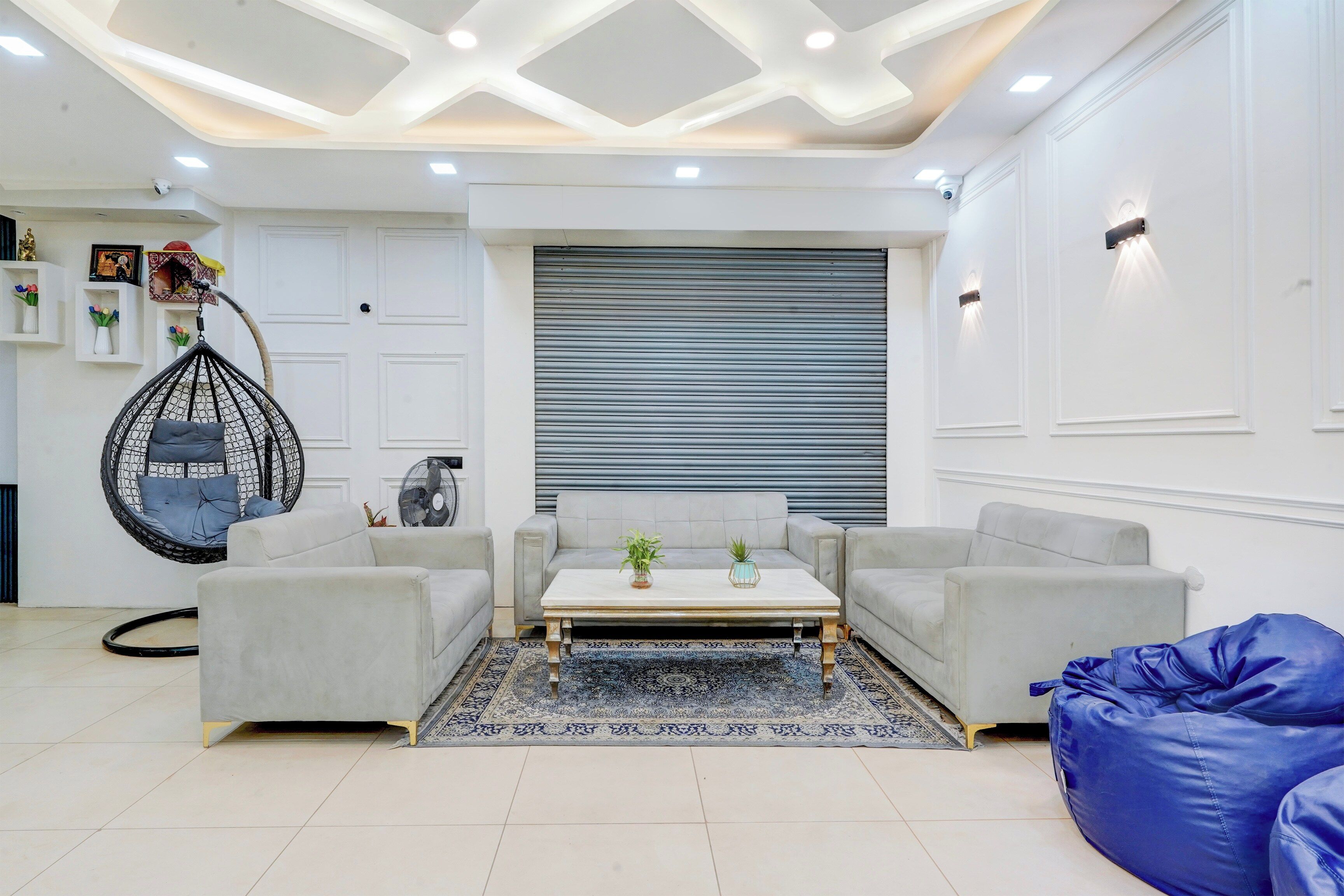 Una sala de estar moderna con un conjunto de sofás, una silla colgante, una mesa de centro y un sillón de pelotas azules.