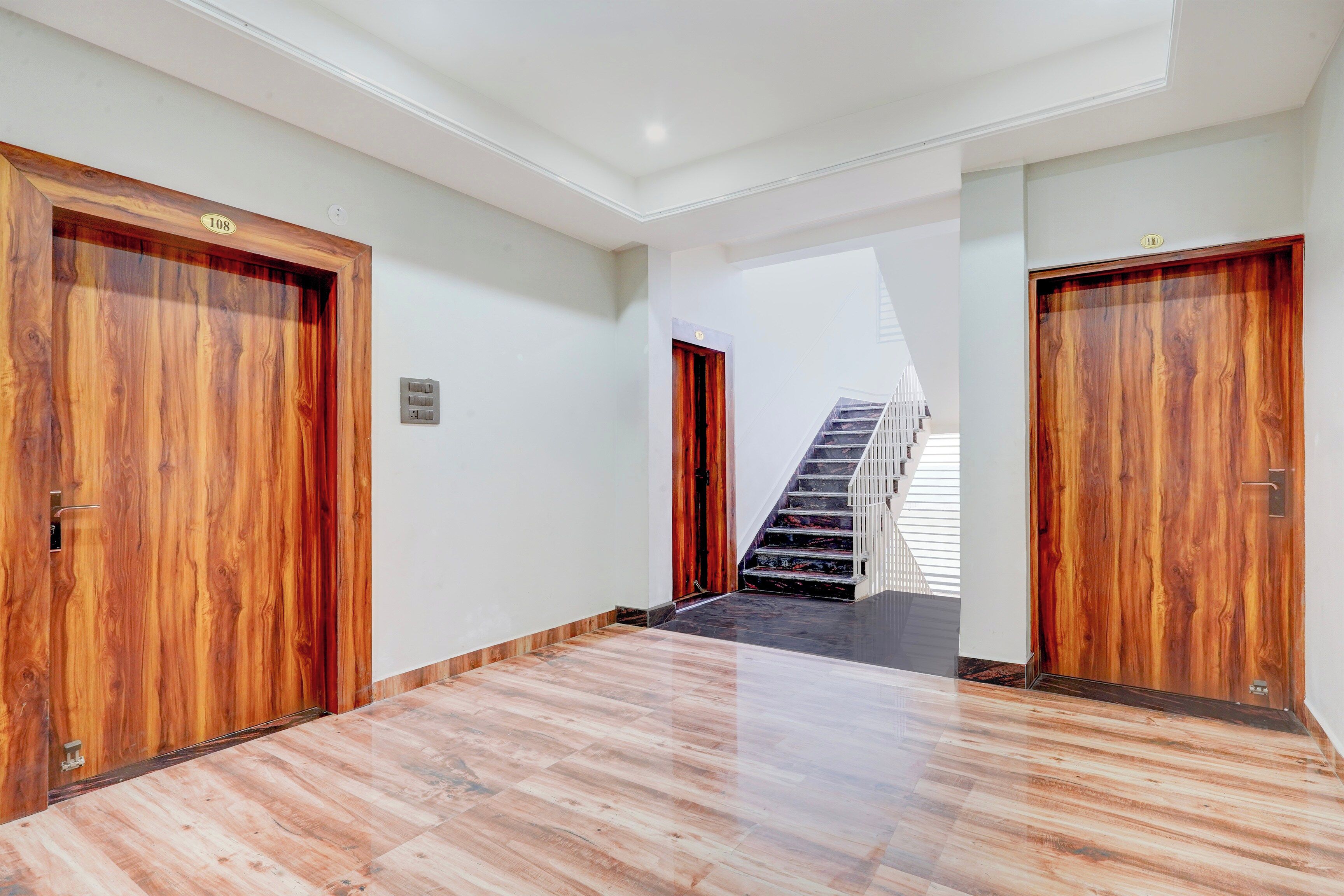 Un pasillo con puertas de madera, una escalera y suelo de baldosas.