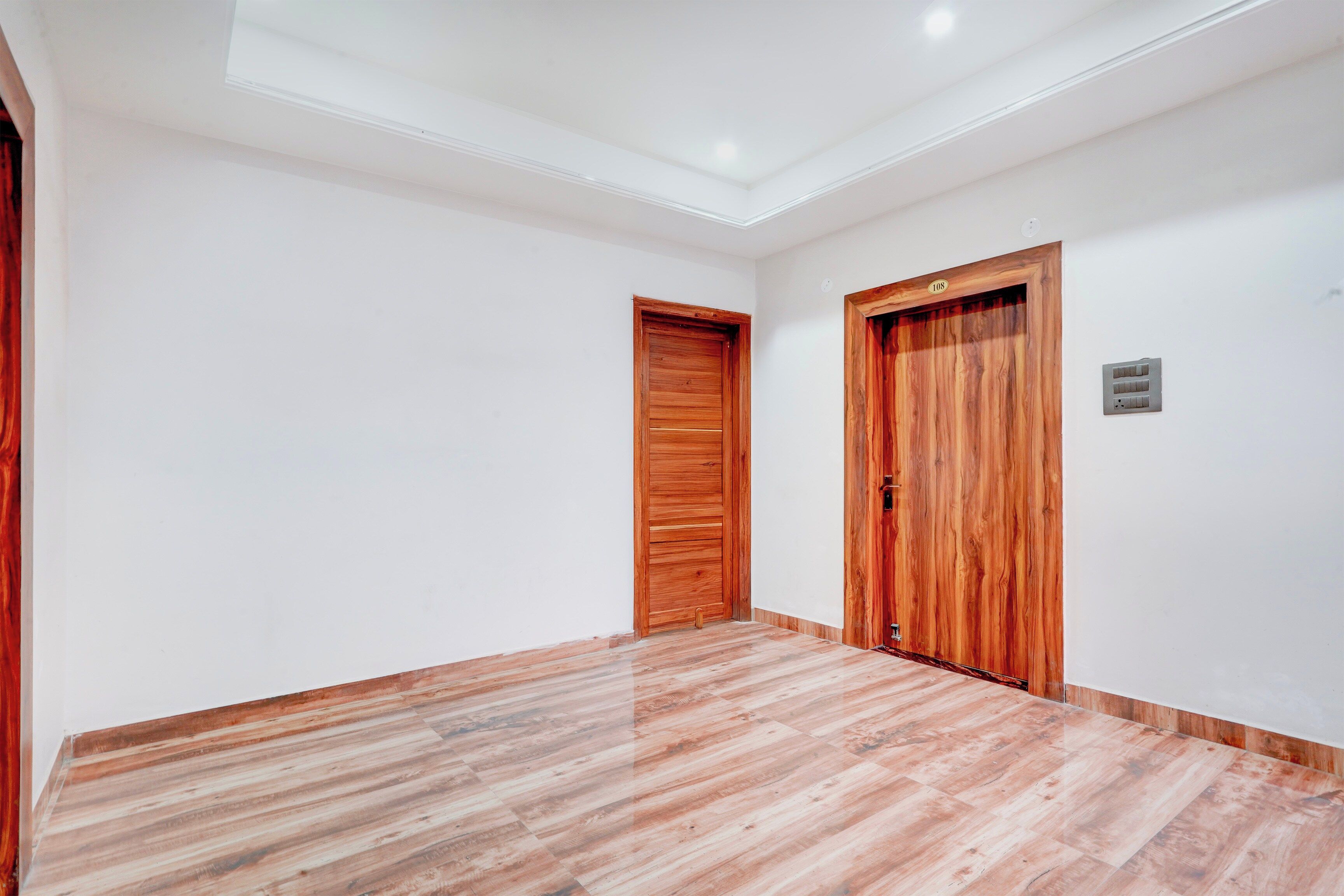 A hallway with wooden doors, a white wall, and a wooden floor.