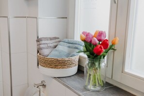 Et badeværelse med et håndklædestativ, en vævet kurv med håndklæder og en vase med tulipaner.