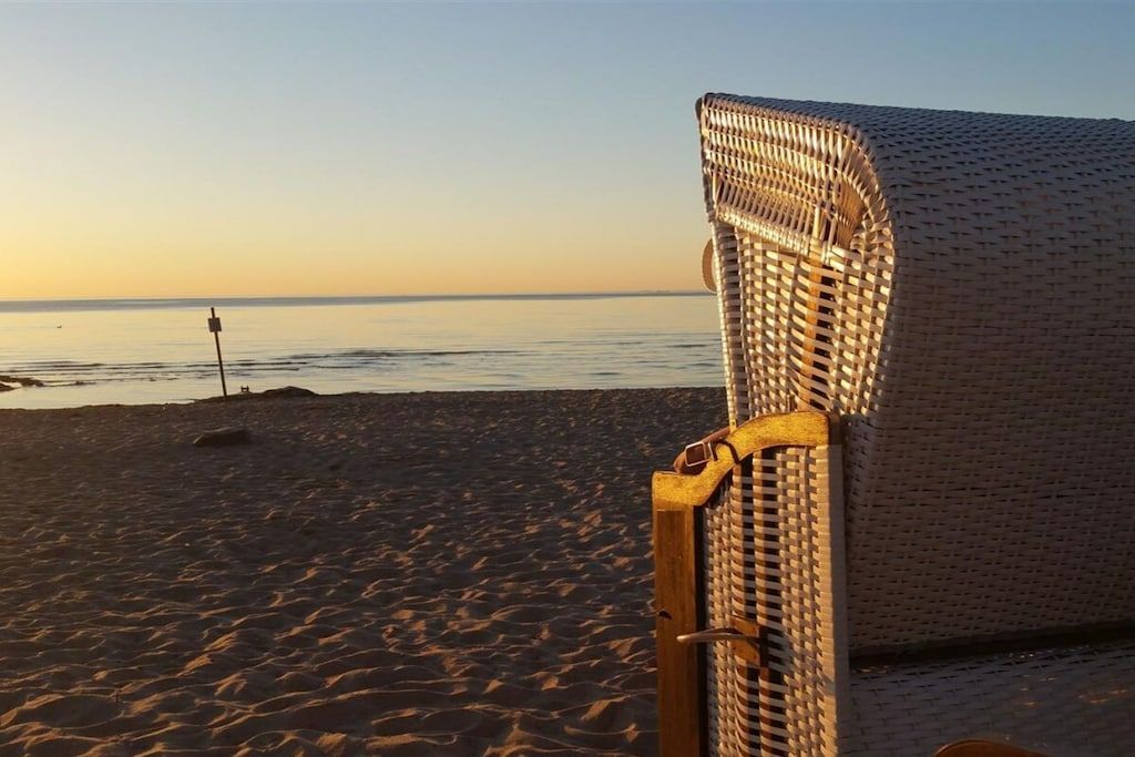 Une scène de plage avec une chaise en osier et un poteau en bois au premier plan.