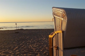 Eine Szene am Strand mit einem Korbstuhl und einem Holzpfosten im Vordergrund.