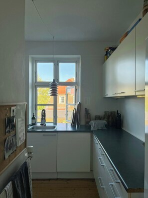 A kitchen with a window, white cabinets, a sink, and a wooden floor. - 1930s flat with a renovated garden in Valby (København)