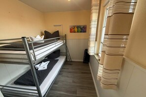 A bunk bed room with a painting on the wall, a window with curtains, and a trash bin. - Bungalow with 1 bedroom (Dornum - Dornumersiel)