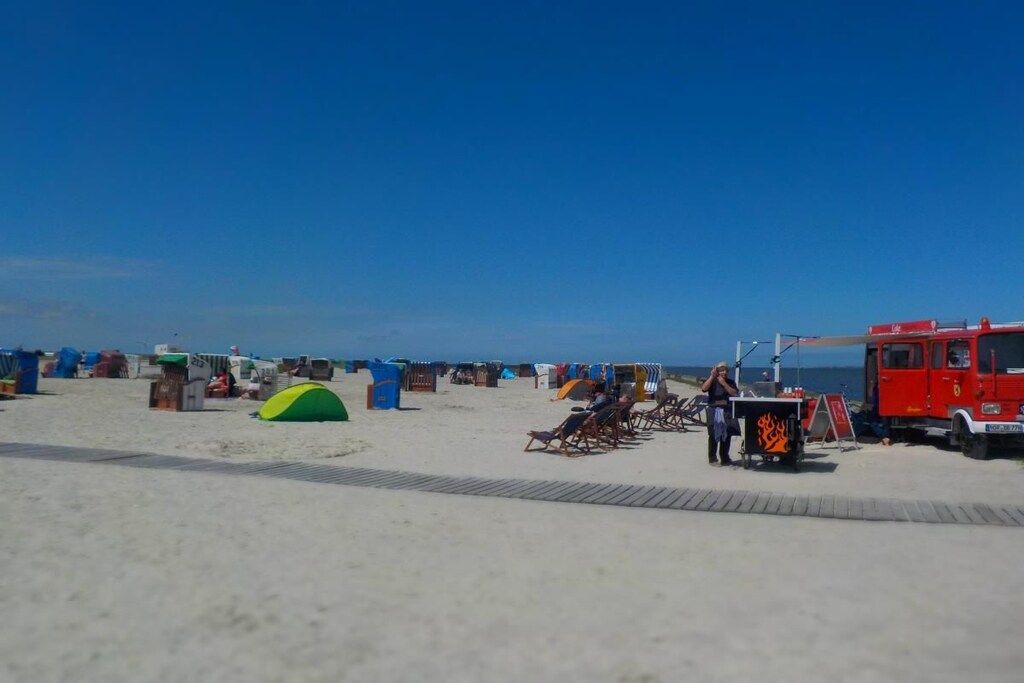 Une plage avec des tentes, un poste de surveillance des sauveteurs et un véhicule rouge.