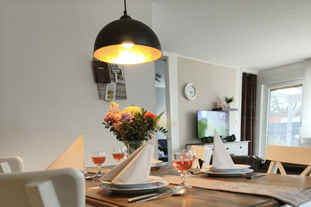 Ein Essbereich mit einem Tisch für zwei Personen, einer Blumenvase und einem Fernseher im Hintergrund.