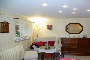A living room with a sofa, a round table, a radiator, a wooden cabinet, and a mirror on the wall. - Holiday apartment with 1 bedroom (Himmelpfort)