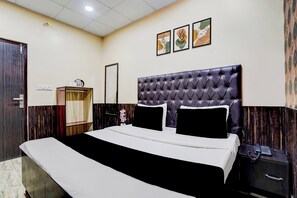 Une chambre d’hôtel avec un grand lit, une armoire en bois, une table de chevet avec un téléphone et un miroir.
