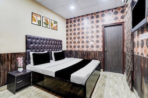 Un dormitorio con cama, mesitas de noche, televisor montado en la pared y un papel tapiz estampado.