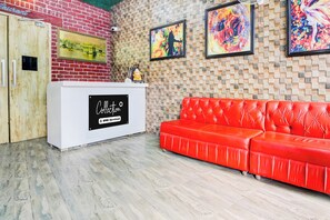 Un espace d’accueil avec un comptoir blanc, un canapé en cuir rouge et un mur de briques orné d’œuvres d’art.