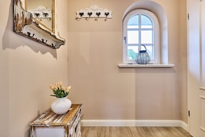 A hallway with a white door, a window with a white frame, a white vase with flowers, and a decorative mirror. - Holiday apartment with 1 bedroom (Rantum)
