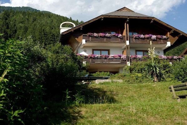 A two-story chalet with balconies adorned with flowers, surrounded by lush greenery and a mountainous backdrop. - Holiday apartment with 2 bedrooms (Millstatt)