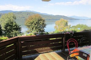 A terrace with a view of a lake and mountains, wooden benches, and a table with chairs. - Holiday apartment with 2 bedrooms (Millstatt)