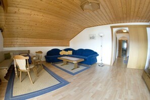 Una sala de estar acogedora con techo de madera, un sofá azul, una mesa de centro de madera y una silla.