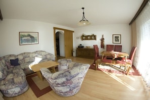 Een woonkamer met een bank, een salontafel en een eethoek met een tafel en stoelen.