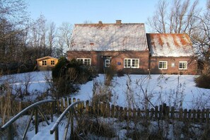 Ein Backsteinhaus mit geneigtem Dach, umgeben von Schnee und einem Holzzaun.