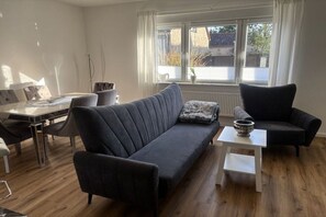 A modern living room with a dark grey sofa, a white coffee table, and a dining area with a table and chairs. - Holiday apartment in Beelitz with Wi-Fi (Beelitz)