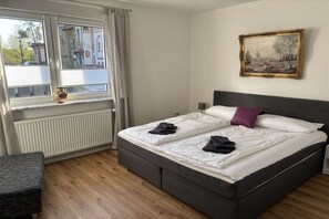 A hotel room with a bed, a window with curtains, a radiator, a painting on the wall, and a small table. - Holiday apartment in Beelitz with Wi-Fi (Beelitz)
