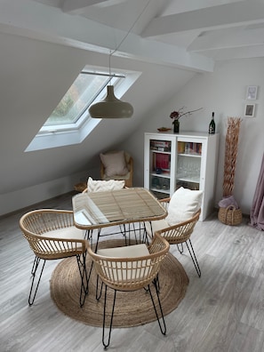 Un coin repas avec une table et des chaises, une bibliothèque et une fenêtre avec un puits de lumière.