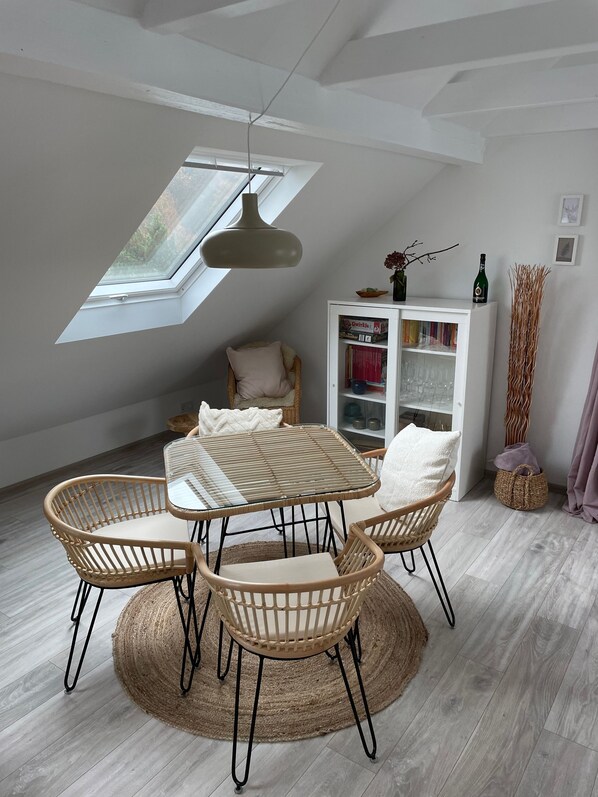 A dining area with a table and chairs, a bookshelf, and a window with a skylight.