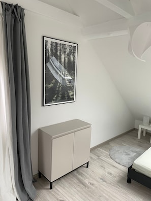 Une chambre à coucher avec un lit, une armoire grise, un tableau encadré représentant une forêt et un rideau gris.