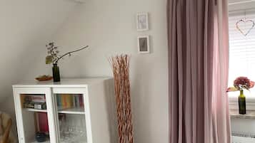 A room with a white cabinet, a tall decorative plant, a pink curtain, and a small basket with a rolled towel.