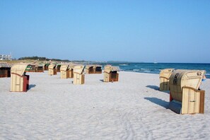 A beach with rows of wicker beach chairs, some with numbers on them, and a clear view of the ocean and a sailboat in the distance. - Holiday apartment with 2 bedrooms (Burg auf Fehmarn)