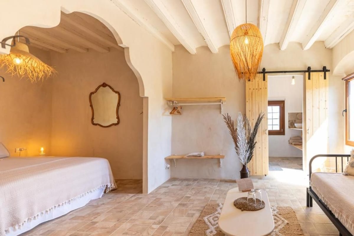 A bedroom with a bed, a bedside table, a hanging light fixture, and a mirror on the wall.