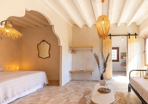 A bedroom with a bed, a bedside table, a hanging light fixture, and a mirror on the wall. - Masia Aubareda (SANT MARTÍ DE TOUS)