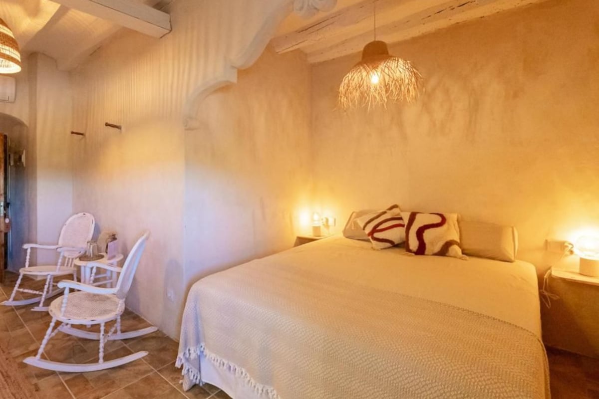 A bedroom with a large bed, two rocking chairs, a hanging light fixture, and a wall-mounted lamp.
