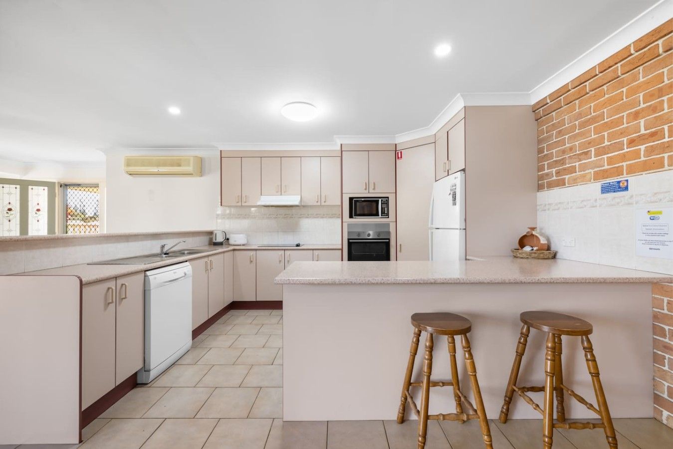 A modern kitchen with a central island, bar stools, and a brick accent wall.