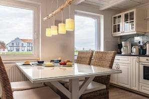 A modern kitchen with a glass dining table, wicker chairs, and a view of the outside. - 50111 Fisherman's Loft (Carolinensiel)